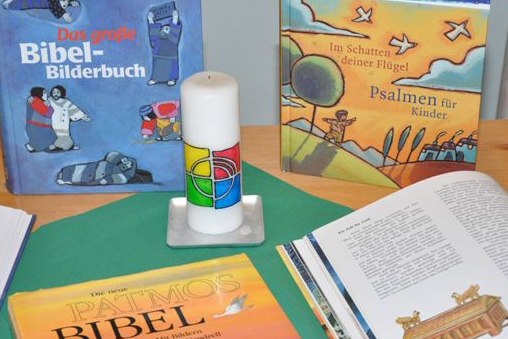 Verschiedene Kinder-Bibelausgaben und eine Kerze stehen auf einem Tisch