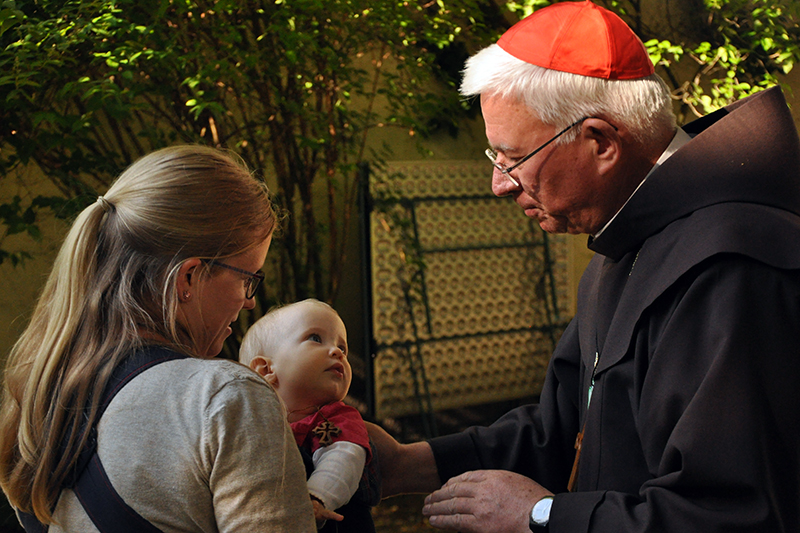 Erzbischof Franz Lackner segnet ein Kind, das von seiner Mutter getragen wird.