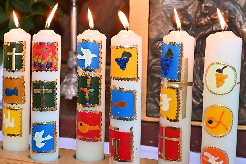 sechs brennende Kerzen mit Glaubenssymbolen