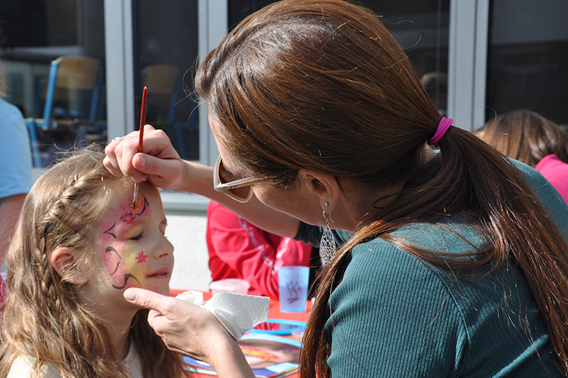 Eine Gruppenleiterin schminkt einem Kind ein Blütenmuster auf das Gesicht